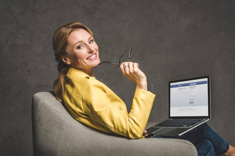 smiling woman using laptop with facebook opened